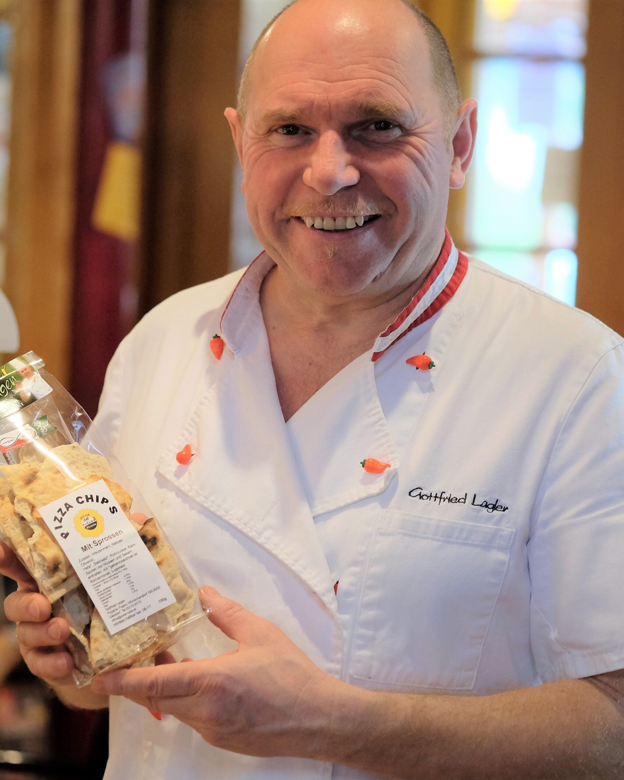 Gottfried Lagler im Kochrock mit einer Packung Pizza-Chips mit Sprossen